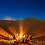 Desert landscape with towering sand dunes, a camel caravan, and a starry night sky.