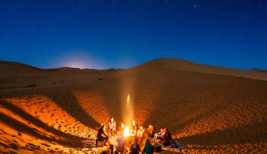 Desert landscape with towering sand dunes, a camel caravan, and a starry night sky.