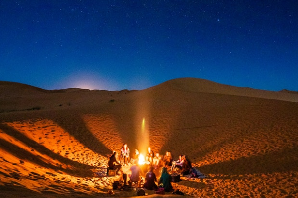Desert landscape with towering sand dunes, a camel caravan, and a starry night sky.